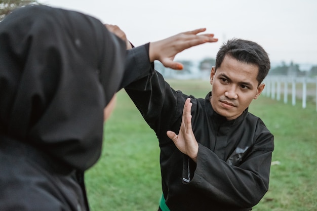 Giovani uomini asiatici che indossano uniformi pencak silat con un movimento di deflessione e donna che indossa un hijab con movimenti colpenti