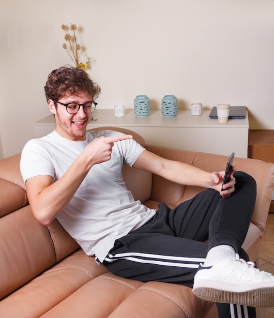 Giovani uomini che fanno videochiamate con il telefono mentre sono seduti sul divano beige a casa