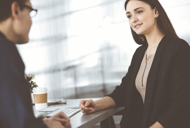 Giovani uomini d'affari amichevoli parlano tra loro, seduti alla scrivania in un ufficio moderno. Concentrati sulla donna. Concetto di successo aziendale.