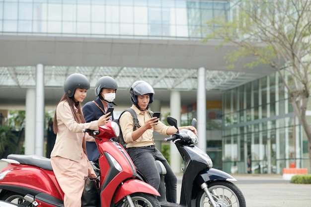 Giovani uomini d'affari asiatici seduti su scooter e leggere notizie importanti sullo smartphone
