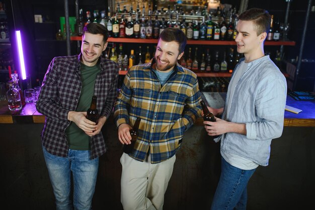 Giovani uomini in abiti casual parlano ridendo e bevendo seduti al bancone del bar nel pub