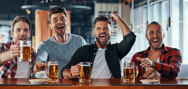Giovani uomini incoraggianti in abbigliamento casual che bevono birra e guardano una partita sportiva