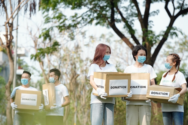 Giovani volontari in maschera medica che lavorano per la fondazione di beneficenza, trasportano scatole con oggetti donati