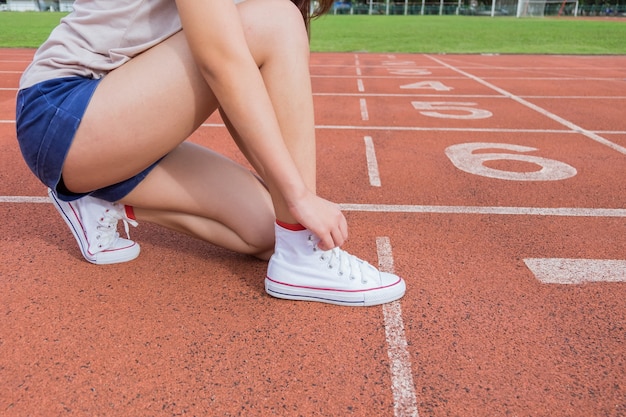 Giovanissimo corridore adolescente che lega i lacci delle scarpe a correre in pista