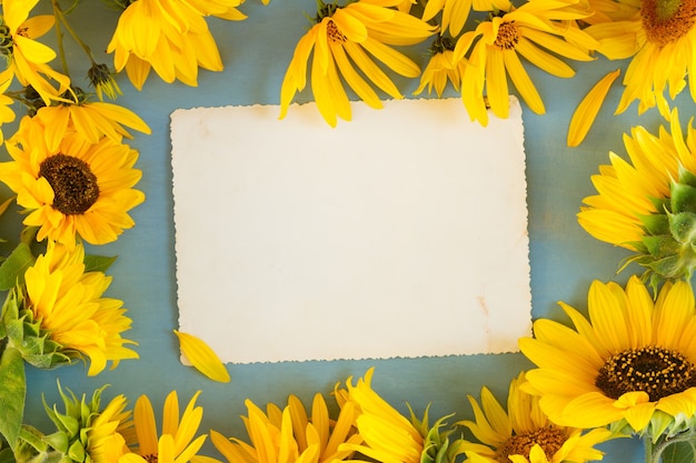 Girasoli su sfondo di legno blu, copia spazio su nota di carta invecchiata, vista dall'alto