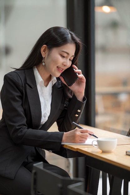 Girato una donna d'affari felice seduta al tavolo di legno e parlando con qualcuno sul suo telefono cellulare durante la pausa dal lavoro