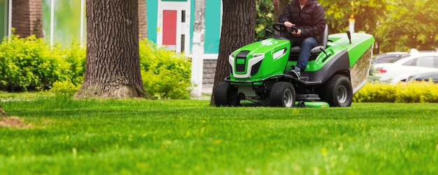 Giro del giardiniere su un trattore che falcia il prato guida e falcia un prato con erba verde nel parco.