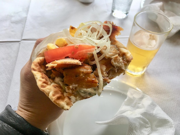 Giroscopi greci con carne Patatine fritte pomodoro cipolla in pita in mano con un bicchiere di birra in Grecia