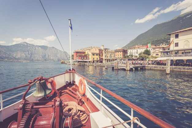 Gita in barca Prua della barca con campana della barca vista sulla catena montuosa delle acque azzurre e sul piccolo villaggio Lago di Garda Italia