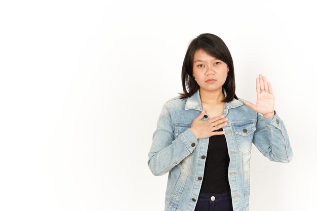 Giuramento di bella donna asiatica che indossa giacca di jeans e camicia nera isolata su sfondo bianco