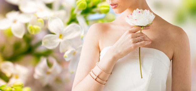 glamour, bellezza, gioielli e concetto di lusso - primo piano di bella donna con anello d'oro e braccialetto che tiene fiore su sfondo di fiori lilla primaverili naturali