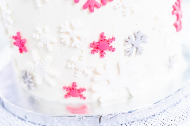 Glassare una torta alta e rotonda con glassa bianca al burro italiano e decorare con fiocchi di neve fondenti.