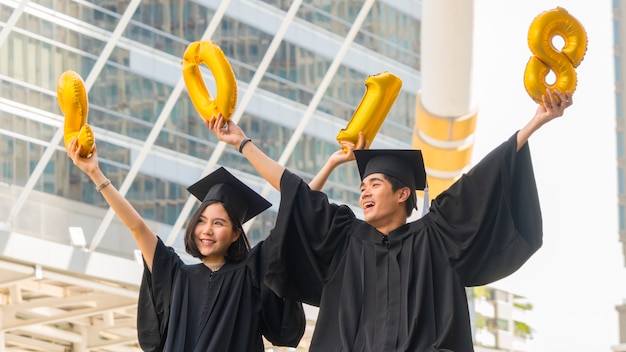 Gli adolescenti laureati felici si siedono con gli abiti di graduazione nella cerimonia di congratulazione con ballon 2018.