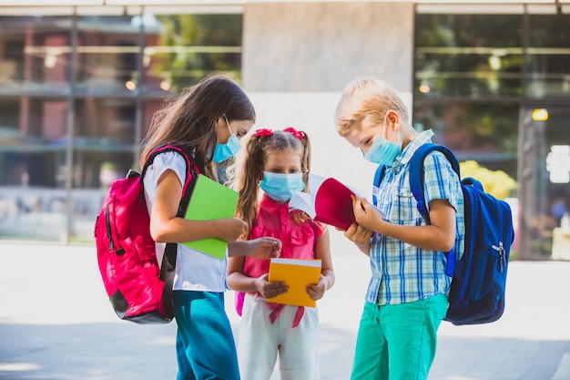 Gli allegri compagni di scuola che chiacchierano all'aperto non riescono a smettere di parlare e tornano a casa I bambini si sono persi durante un lungo periodo di blocco Indossando una maschera medica nel concetto di luoghi pubblici