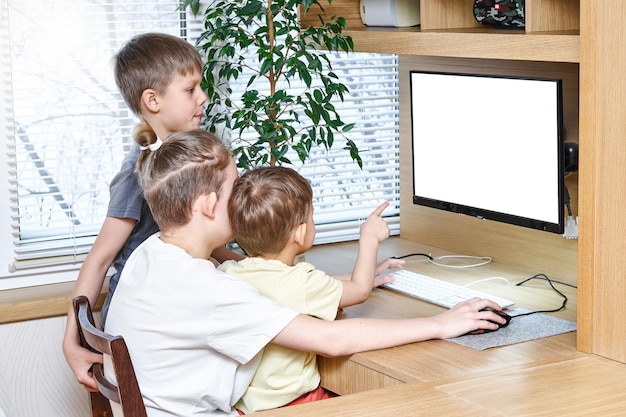 Gli alunni del ragazzo si siedono sulla sedia alla scrivania del computer in legno che esamina il monitor bianco