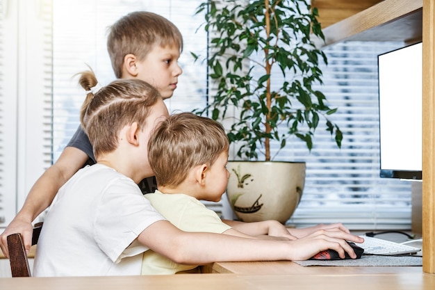 Gli alunni del ragazzo si siedono sulla sedia alla scrivania del computer in legno che esamina il monitor bianco