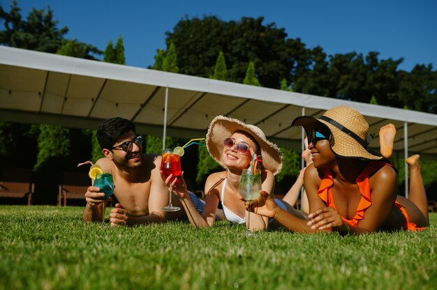 Gli amici allegri riposano sull'erba vicino alla piscina