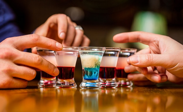 Gli amici bevono shot o liquore. Cinque bicchieri di alcol. Shot di tequila, vodka, whisky, rum. Aperitivo in discoteca. Gruppo di amici bicchierini di tequila al bar. Il maschio passa bicchieri di shot o liquore.