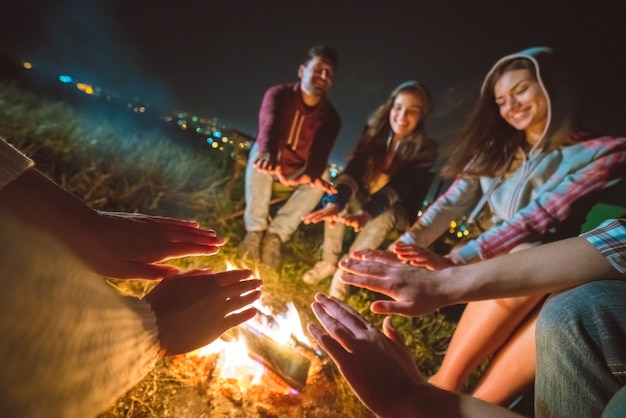 Gli amici felici che si scaldano vicino al falò. sera notte