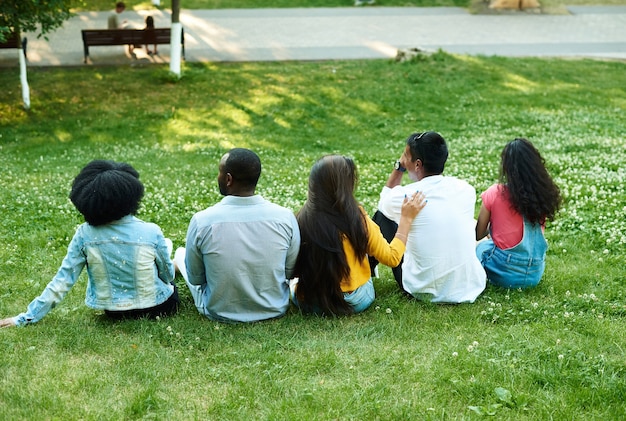 Gli amici multietnici sono seduti sull'erba nel parco.