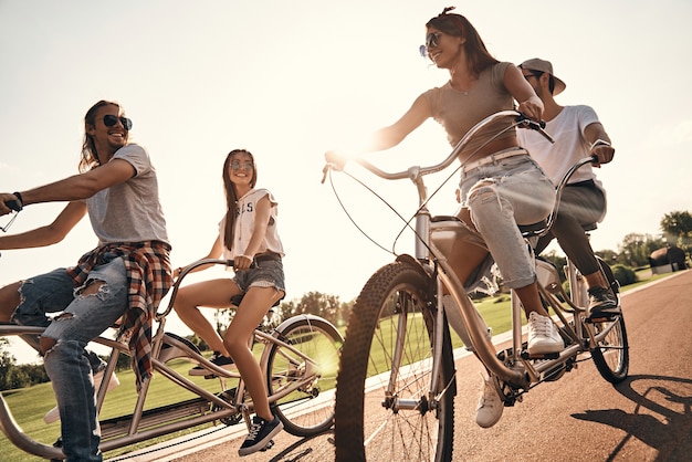Gli amici si rendono felici. Gruppo di giovani felici in abbigliamento casual che sorridono mentre vanno in bicicletta insieme all'aperto