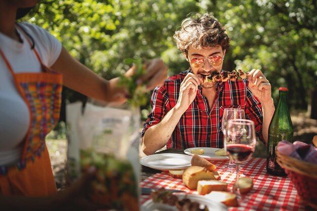 Gli amici si riuniscono al gruppo picnic di giovani che mangiano spiedini di carne