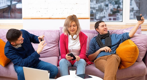 Gli amici si siedono sul divano in chat e utilizzano un computer portatile per smartphone