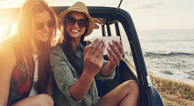 Gli amici sorridono e il selfie del telefono in viaggio con il tramonto per le vacanze di viaggio, le vacanze estive e il relax insieme all'aperto Donne felici e la fotografia dello smartphone per l'avventura o il sole in campagna