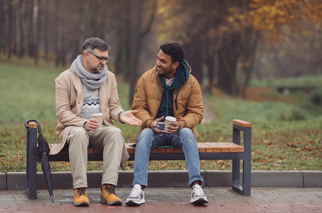 Gli amici un anziano e un giovane si siedono nel parco su una panchina e parlano nel parco autunnale