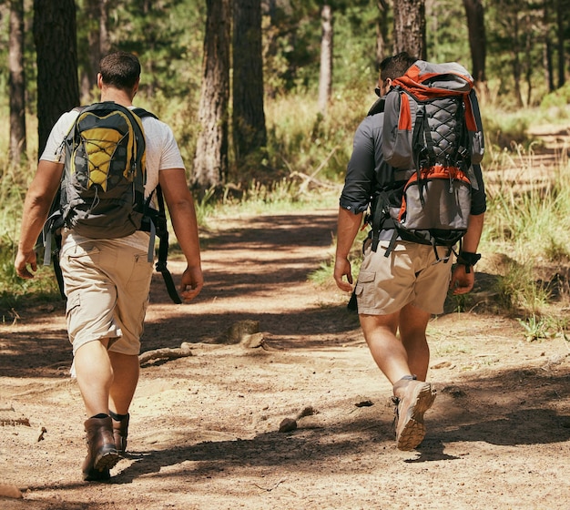 Gli amici zaino in spalla esplorano la natura mentre fanno un'escursione in una foresta insieme, essendo attivi e legando all'aperto Uomini attivi su un sentiero nei boschi che si godono una sfida fisica durante un'avventura di trekking