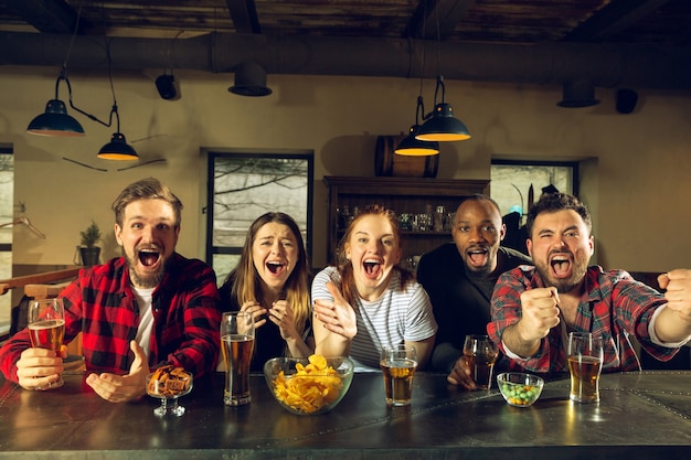 Gli appassionati di sport fanno il tifo al bar pub e bevono birra mentre sta andando la competizione del campionato