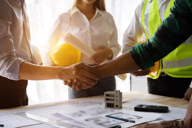 Gli architetti e gli ingegneri dei lavoratori edili si stringono la mano mentre lavorano per il lavoro di squadra e la cooperazione dopo aver completato un accordo in un concetto di cooperazione di successo della struttura dell'ufficio