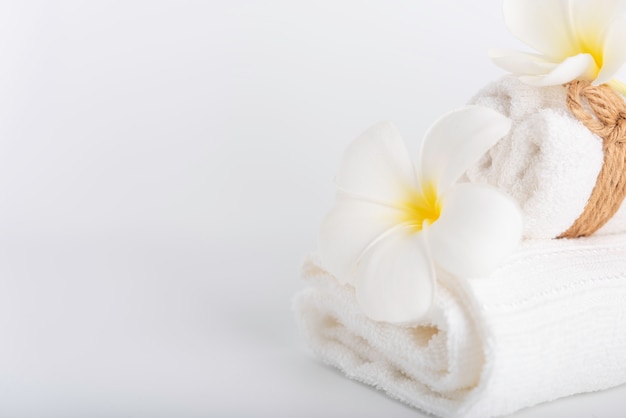 Gli asciugamani rotolati bianco decorano con l&#39;oggetto della stazione termale dei fiori del frangipane su bianco