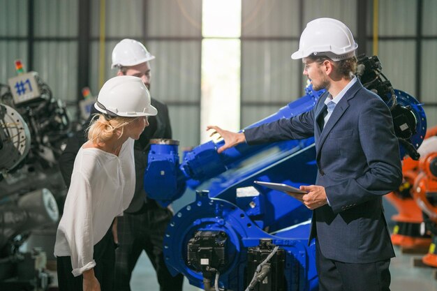 Gli ingegneri aziendali si incontrano e controllano il controllo del braccio del robot della macchina pesante Squadra diversificata di ingegneri di robotica industriale riuniti intorno alla macchina L'operatore di macchinari professionali utilizza il tablet digitale industriale