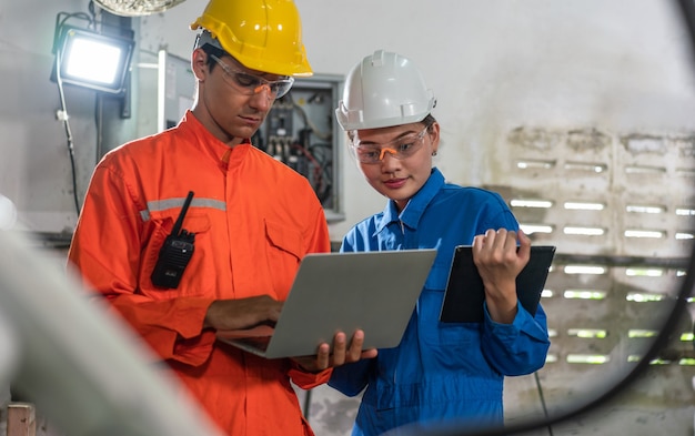 Gli ingegneri dell'automazione maschili e femminili indossano un'uniforme con l'ispezione di sicurezza del casco controllano una saldatrice a braccio robot con un laptop in una fabbrica industriale. Concetto di intelligenza artificiale.