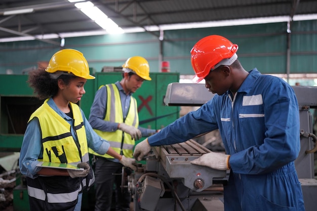 Gli ingegneri industriali maschi e femmine parlano con l'operaio di fabbrica su sfondo di macchine e attrezzature. Lavorano presso l'impianto di produzione dell'industria pesante.