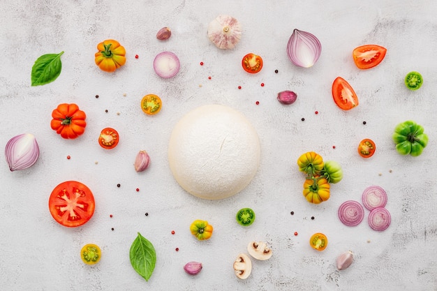 Gli ingredienti per la pizza fatta in casa allestiti su sfondo di cemento bianco.