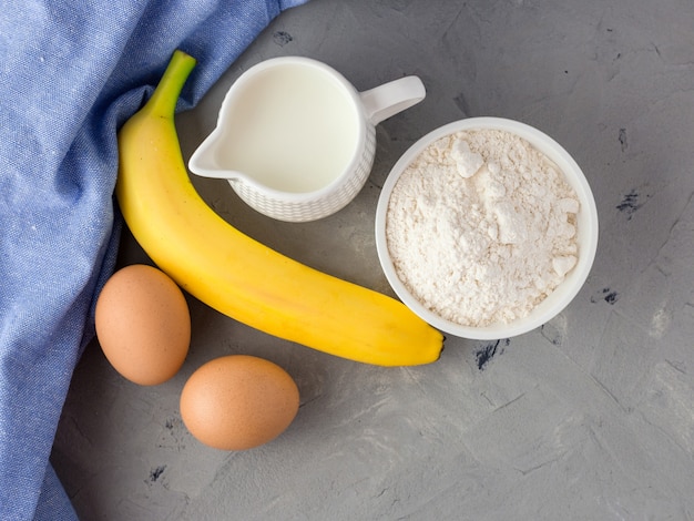 Gli ingredienti per la torta di banana sulla superficie grigia. Cucchiaio Di Legno, Banana, Uova, Latte