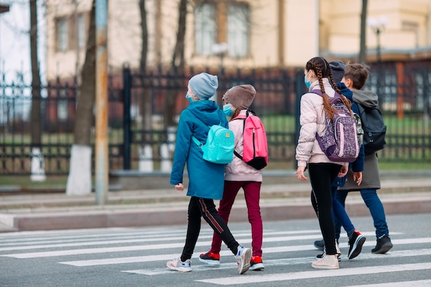 Gli scolari attraversano la strada in maschere mediche. I bambini vanno a scuola.