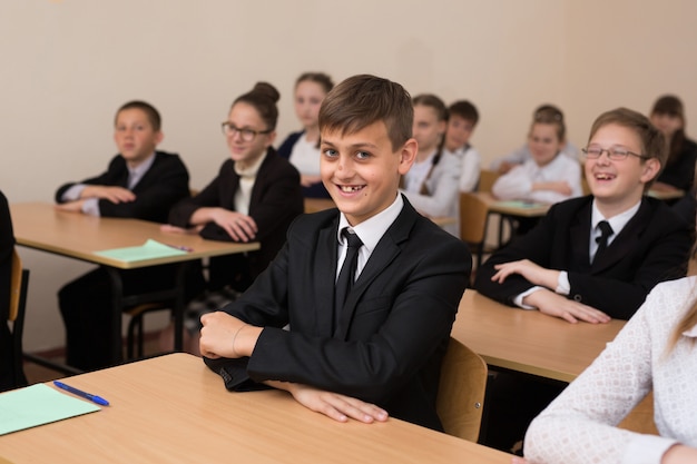 Gli scolari felici si siedono ad una scrivania in classe