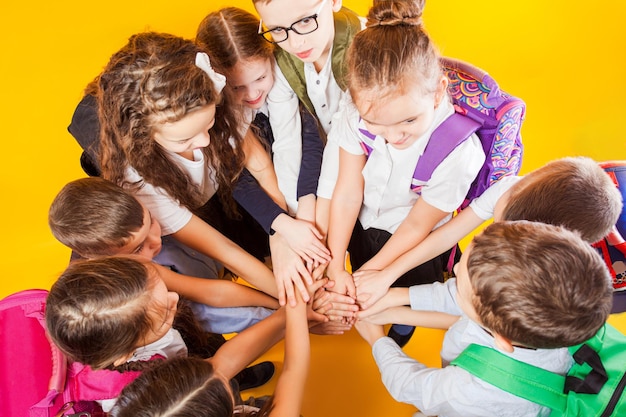 Gli scolari stanno impilando le mani insieme sullo sfondo giallo