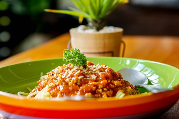 Gli spaghetti con carne di maiale macinata e salsa di pomodoro sembrano gustosi su un piatto di ceramica colorato decora con piante verdi