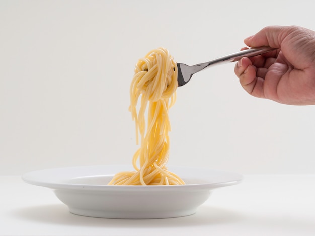 Gli spaghetti della pasta del rotolo della tenuta della mano con una forcella e bish