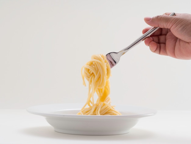 Gli spaghetti della pasta del rotolo della tenuta della mano con una forcella e bish