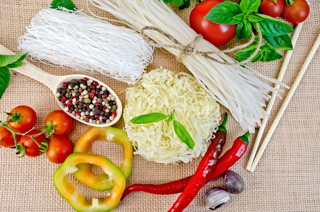 Gli spaghetti di riso sono diversi, pomodori, peperoni, bacchette, aglio, basilico su uno sfondo di tela di sacco