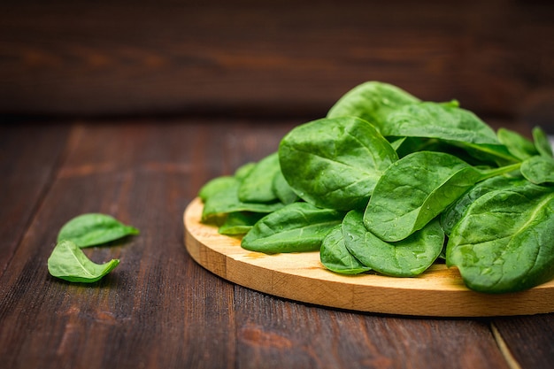 Gli spinaci succosi freschi va su una tavola marrone di legno. Prodotti naturali, verdure, cibo sano