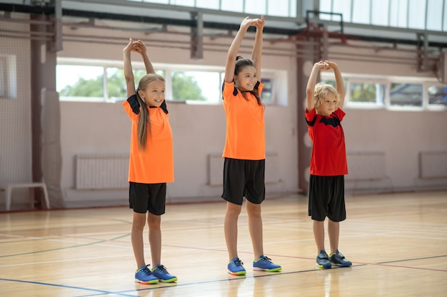 Gli sport. Tre bambini che fanno stretching sulla lezione di ginnastica