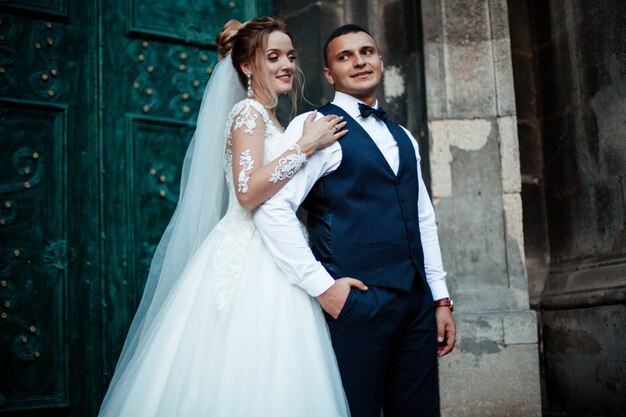 Gli sposi camminano insieme nel parco. Sposa affascinante in un abito bianco, lo sposo è vestito con un abito elegante scuro.