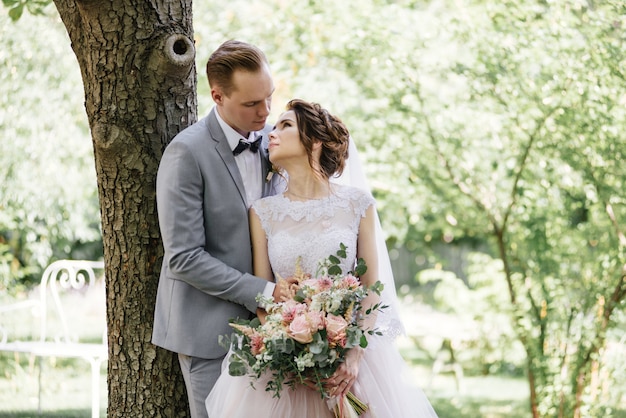 Gli sposi camminano nel giardino. Matrimonio nella foresta. Abito lussureggiante rosa e abito grigio, papillon.