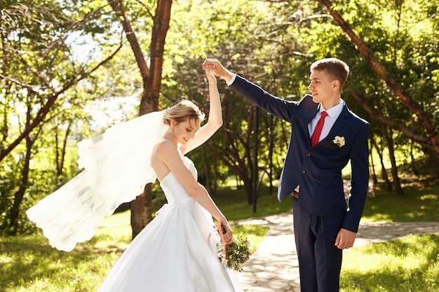 Gli sposi camminano nella natura nel Parco dopo la cerimonia nuziale. Un bacio e un abbraccio da un uomo e una donna. Lo sposo tiene in braccio la sua sposa